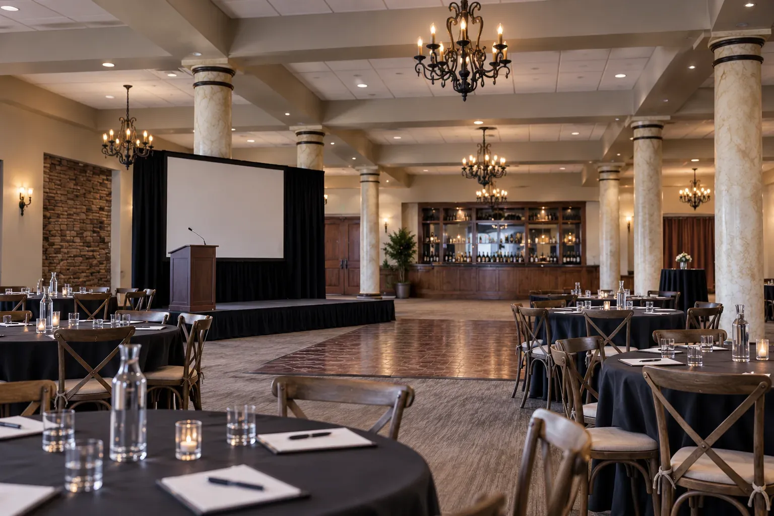 Elegant event ballroom with round tables, stage with projection screen, podium, chandeliers, and bar at Wilson Creek Winery.