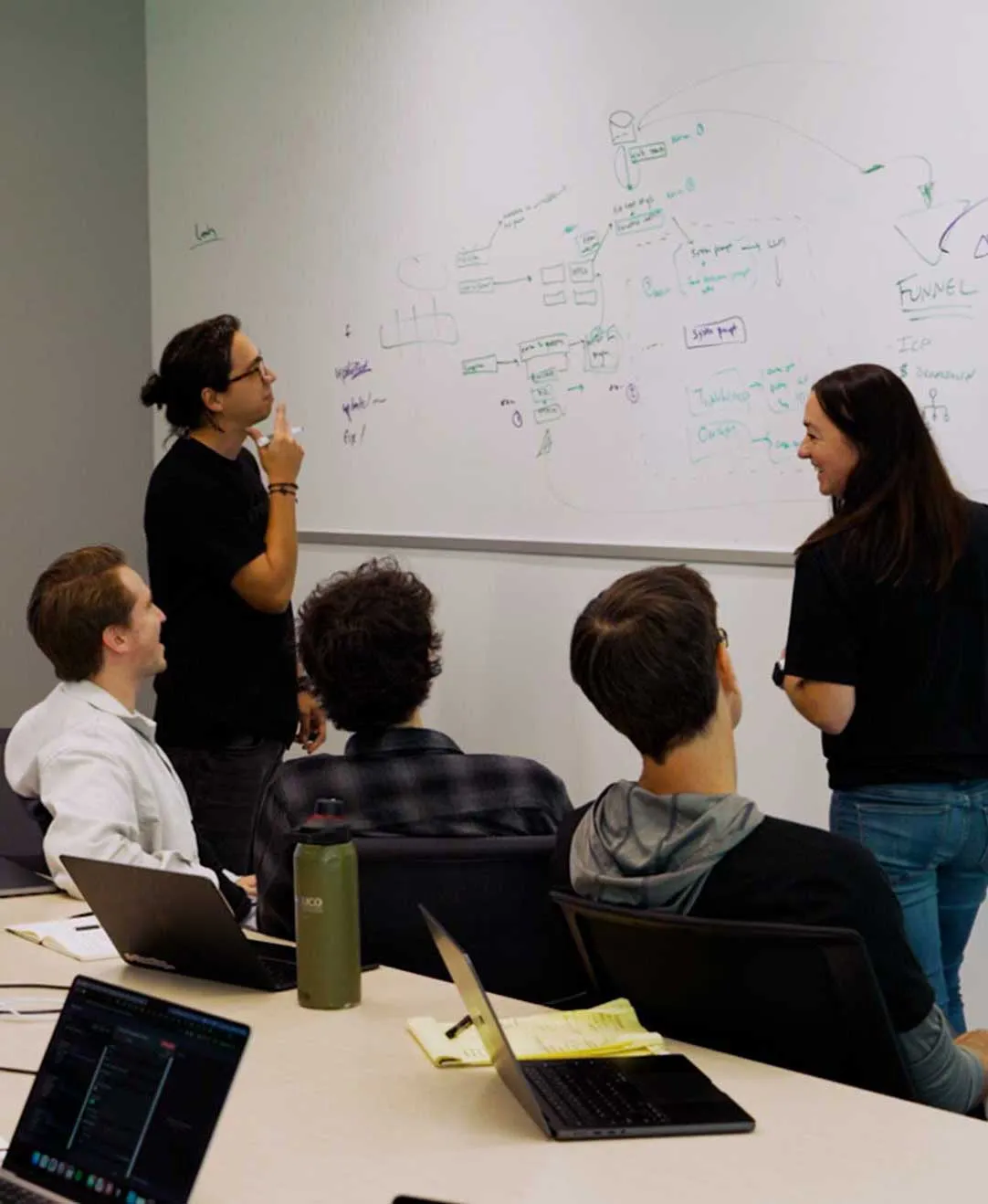 Cadre AI team working at a table in the office, two of them sketching a systems diagram on a whiteboard